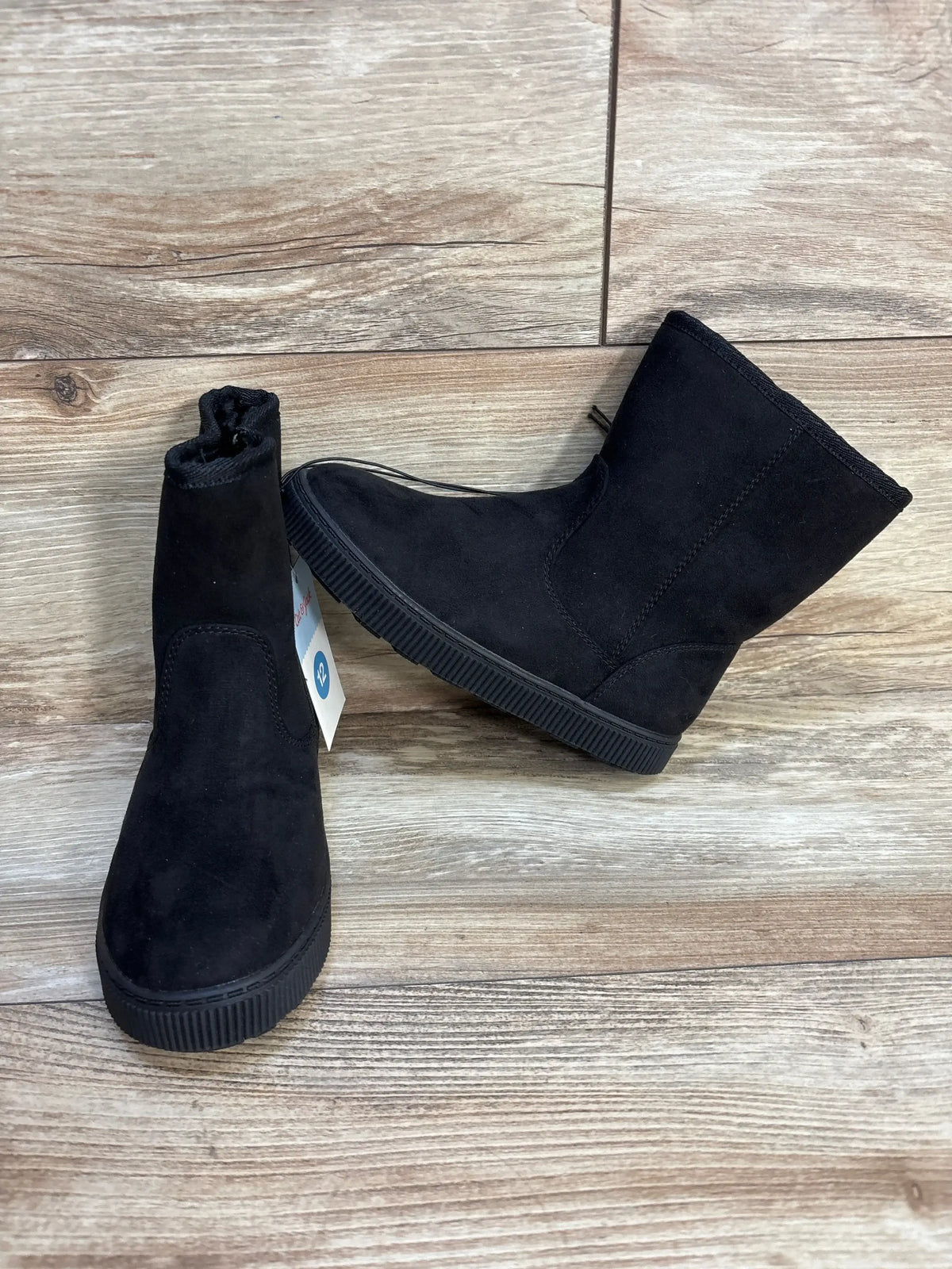 Front and side view of Cat and Jack Pip shearling-style kids boots in black, faux-suede upper and ribbed rubber sole, size 12C tag visible on wood floor