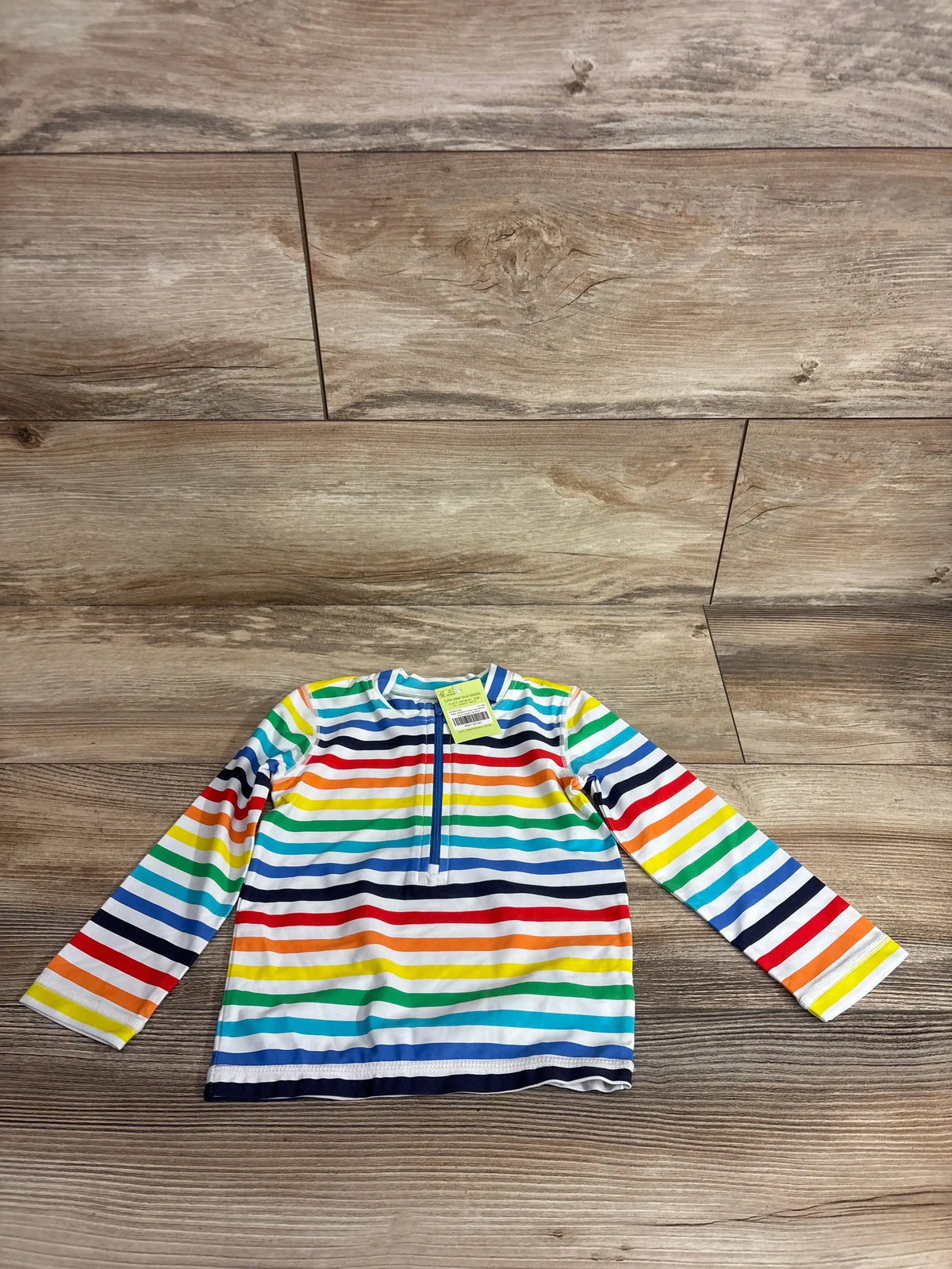 Flat lay of Primary baby long sleeve rash guard with rainbow stripe pattern and half zip neckline on wood plank floor