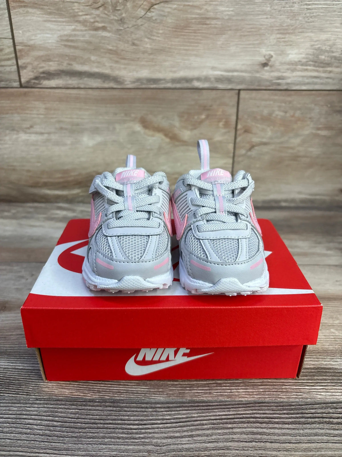 Front view of Nike Vomero 5 TD toddler sneakers, grey with soft pink accents, size 4C, on red Nike box