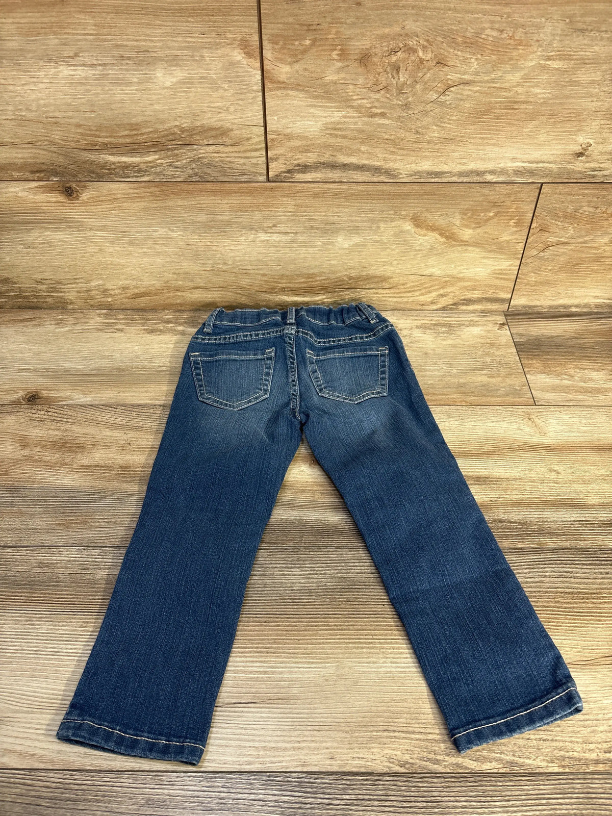 Back view of Children’s Place blue skinny jeans in size 3T showcasing two back pockets on wood flooring