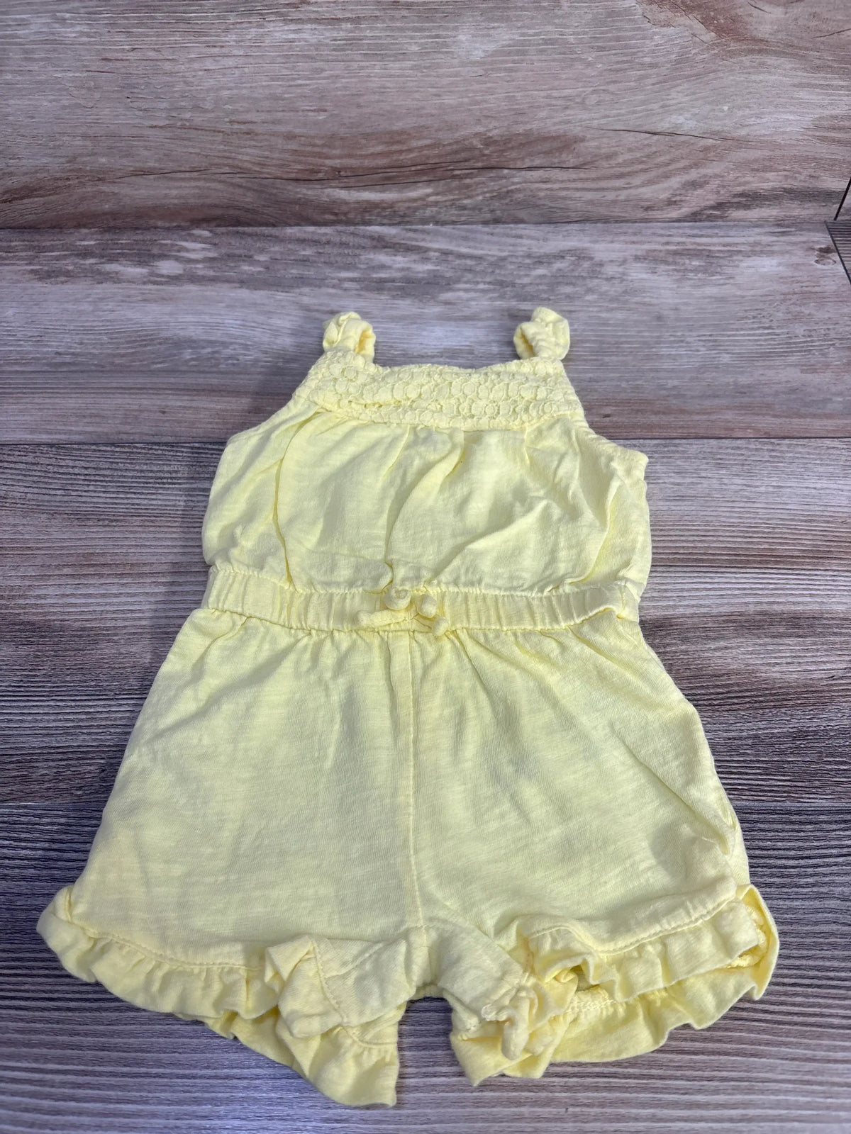 Flat-lay of Carter’s yellow shortie romper with smocked top, knotted straps, elastic waist and ruffle hem on wood