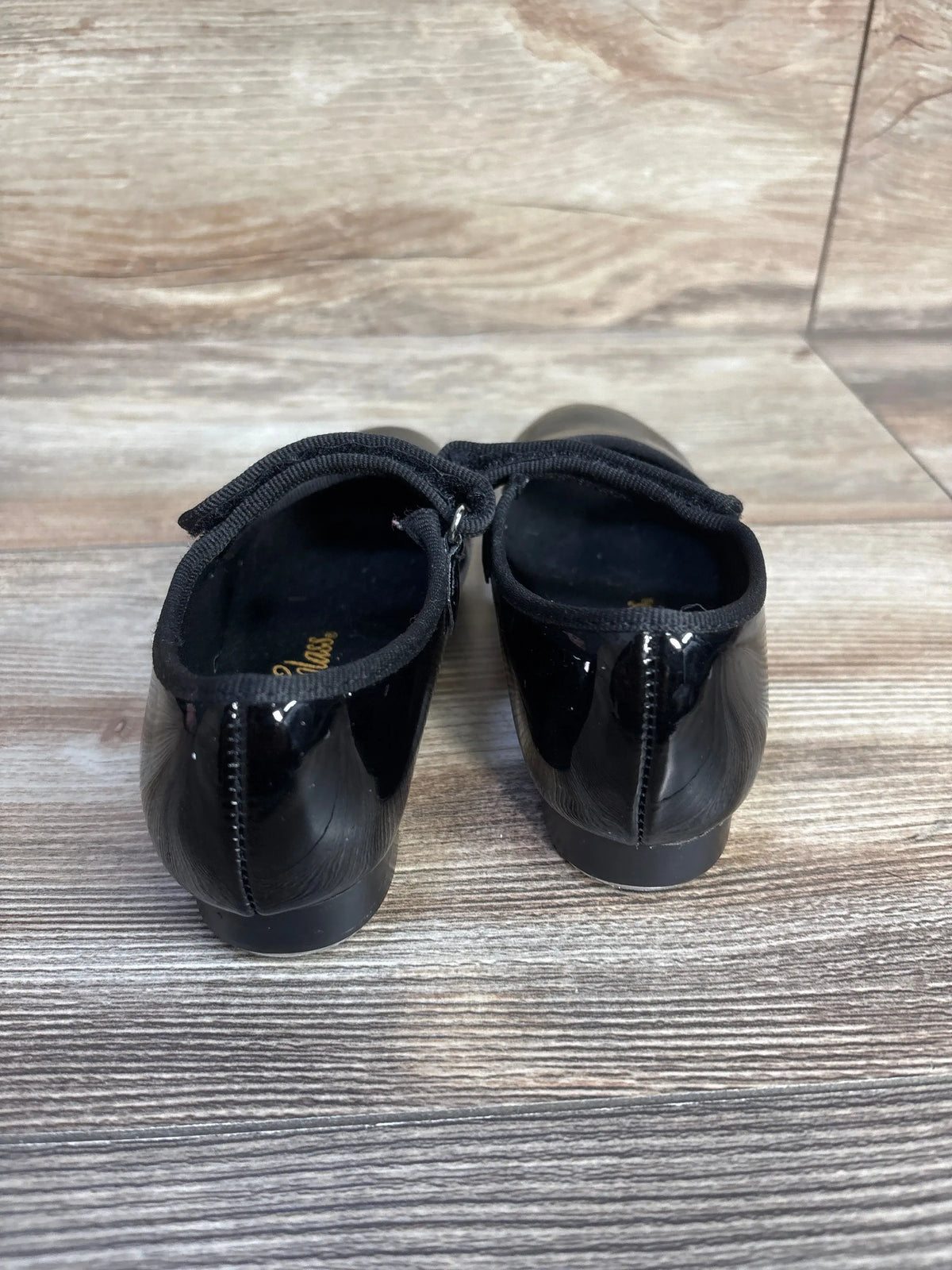Rear view of black patent leather Dance Class tap shoes for kids on a wooden surface
