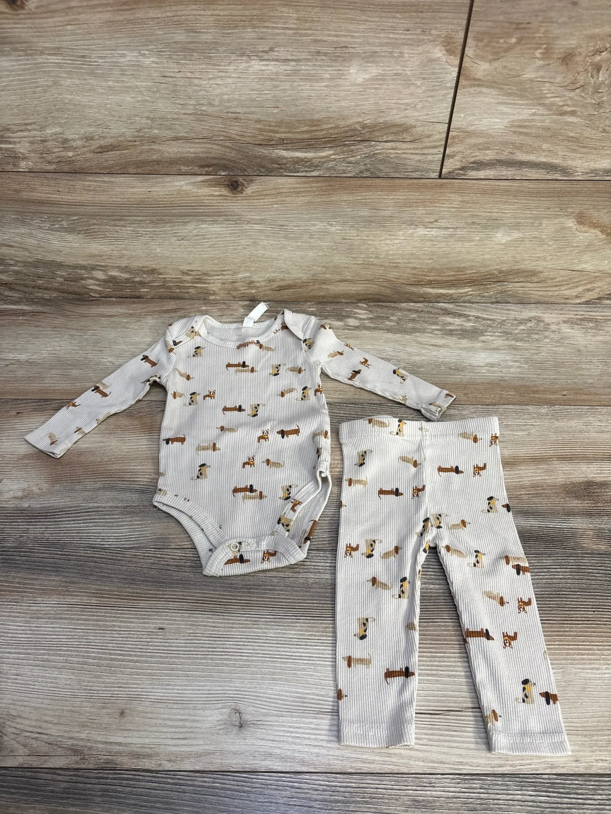 Flat lay of 2-piece ribbed dog-print baby bodysuit and matching pants set in beige, size 3-6 months on wood background