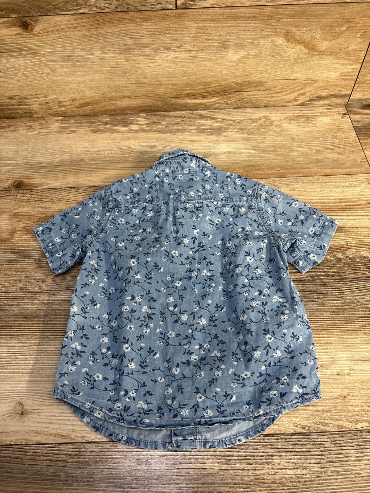 Back view of Janie & Jack blue floral chambray button-down shirt showcasing shirttail hem on a wood floor