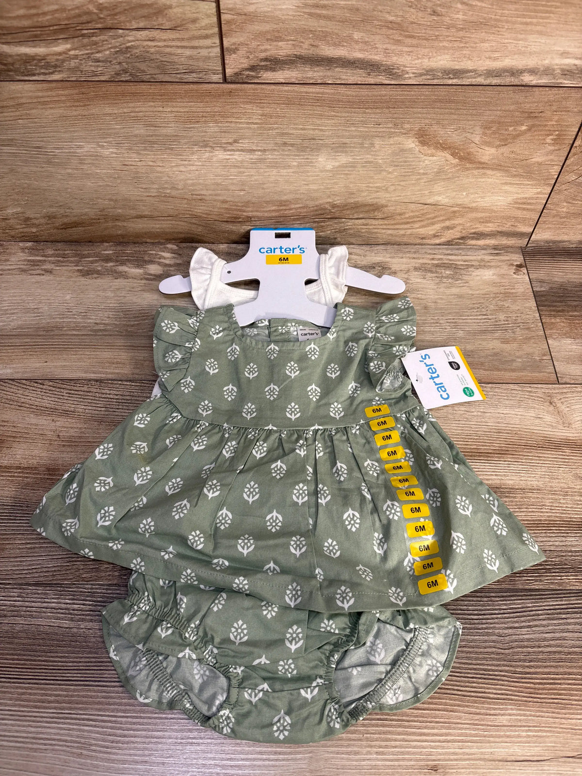 Front view of Carter’s three-piece green floral dress set with ruffled sleeves and matching diaper cover on a wood floor