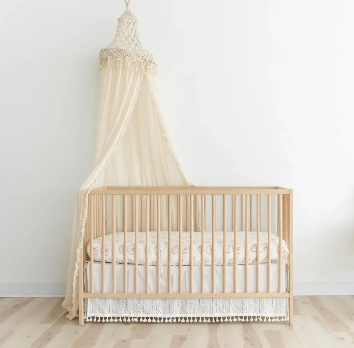 Front view of cream macrame crib canopy with knotted crown and draped fabric over a natural wood crib