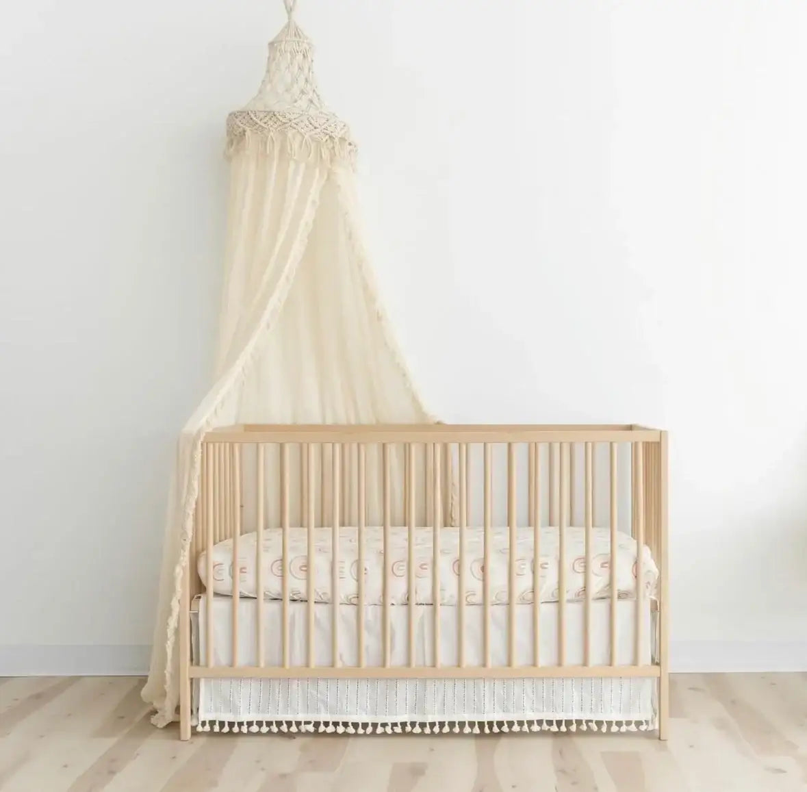 Front view of cream macrame crib canopy with knotted crown and draped fabric over a natural wood crib