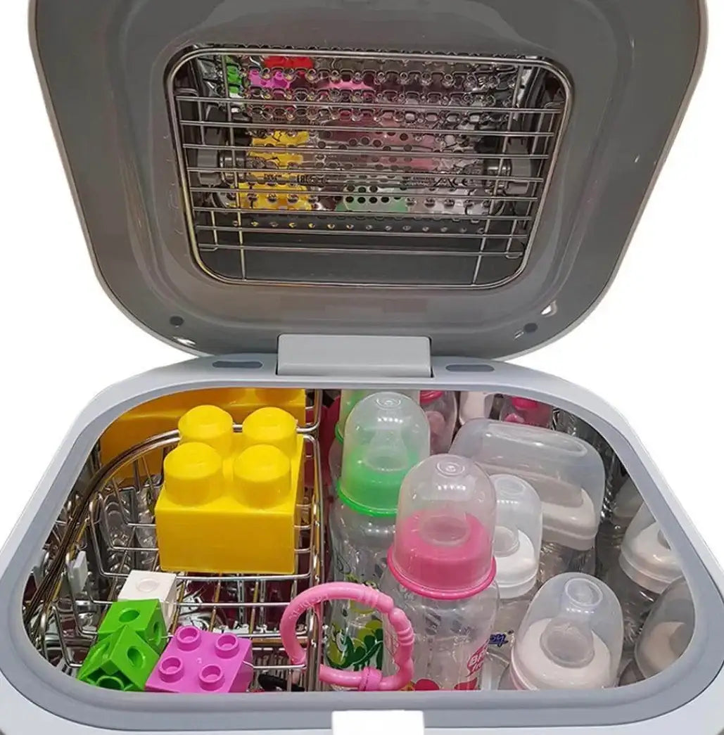Top-down view of UV Care Multipurpose Sterilizer Lite 1 with open lid and stainless-steel rack holding baby bottles, bottle caps, a pink teether ring, and colorful toy blocks