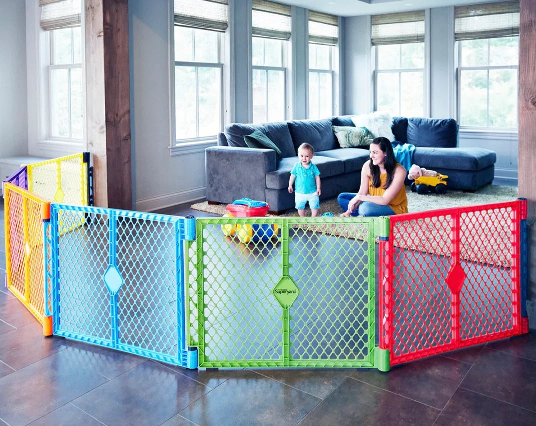 Colorful plastic baby play yard gate set up in a living room with a toddler and adult