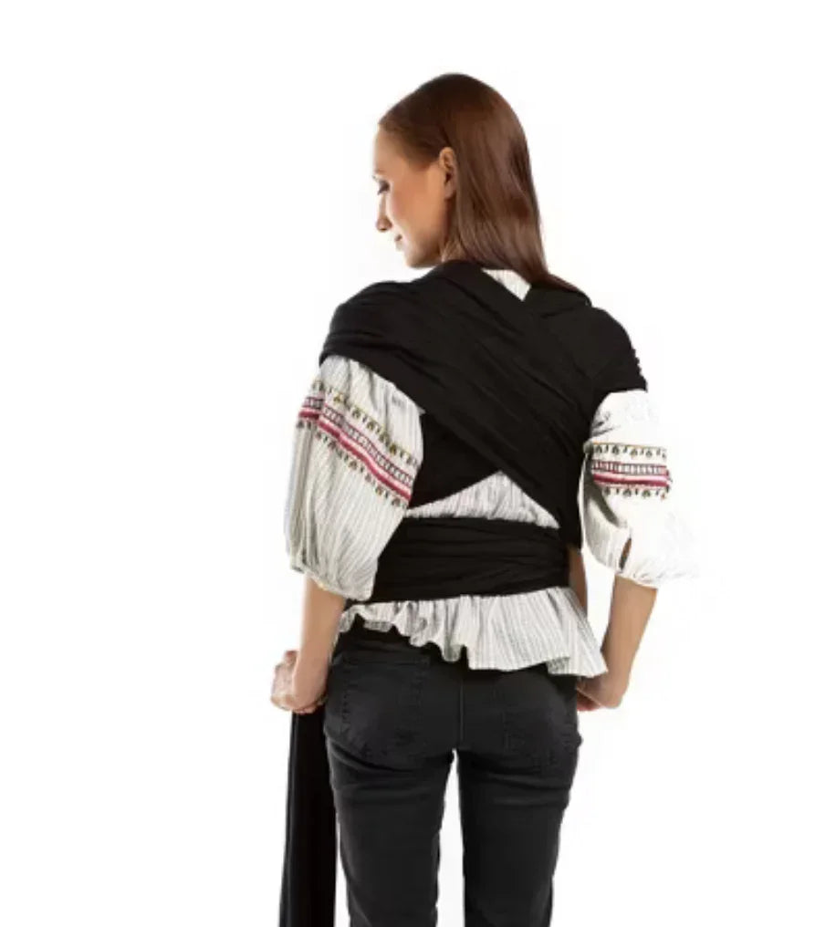 Woman wearing black baby wrap carrier over peasant blouse, rear view on white background