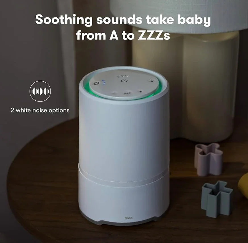 Lifestyle view of Frida Baby 3 in 1 air purifier sound machine and nightlight in white with green glow ring on nursery side table