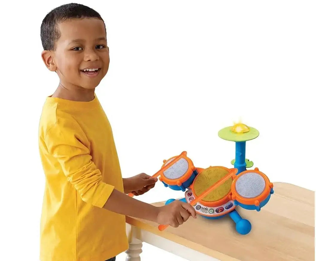 Smiling child in yellow shirt playing with colorful toy drum set on table