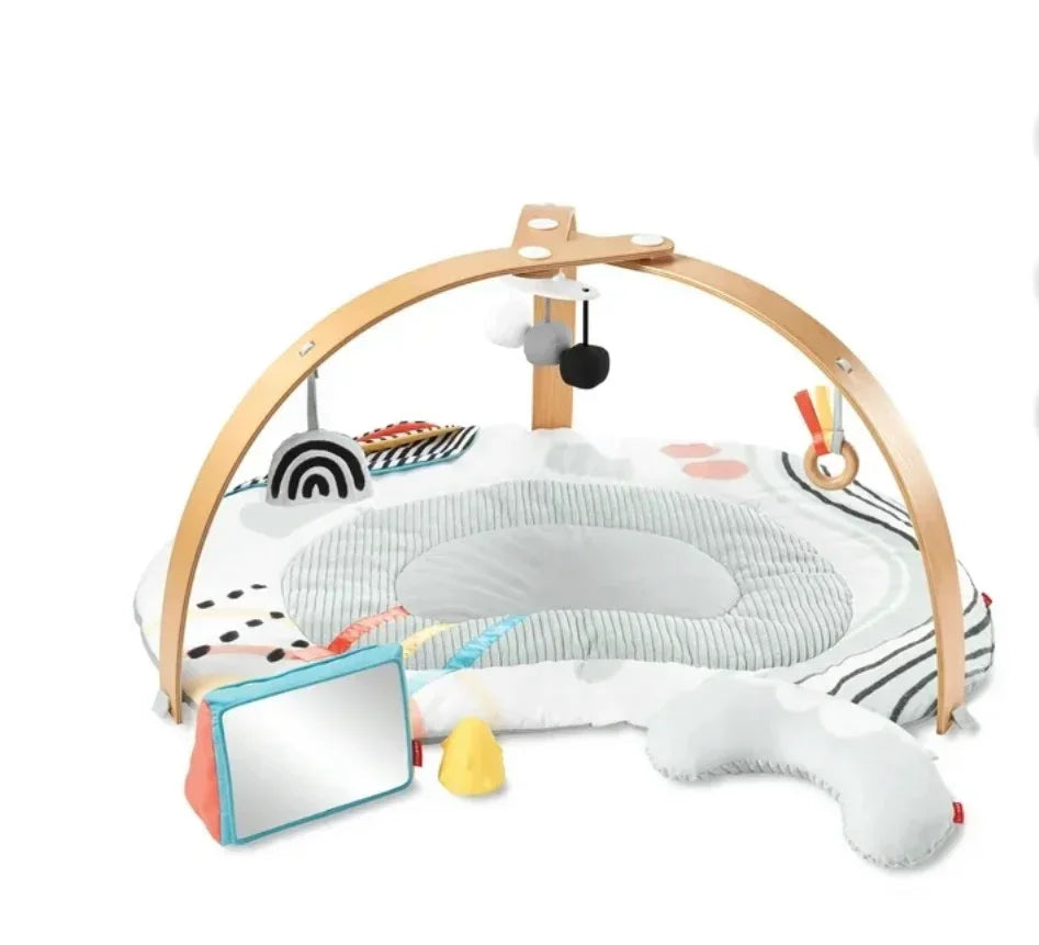 Three-quarter view of Skip Hop Discoverosity play gym with wooden arch, padded mat, head pillow and hanging toys on white
