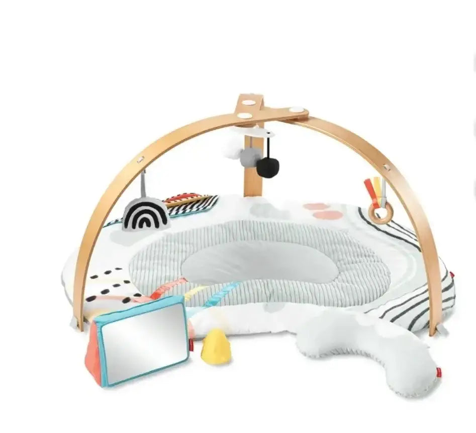 Three-quarter view of Skip Hop Discoverosity play gym with wooden arch, padded mat, head pillow and hanging toys on white