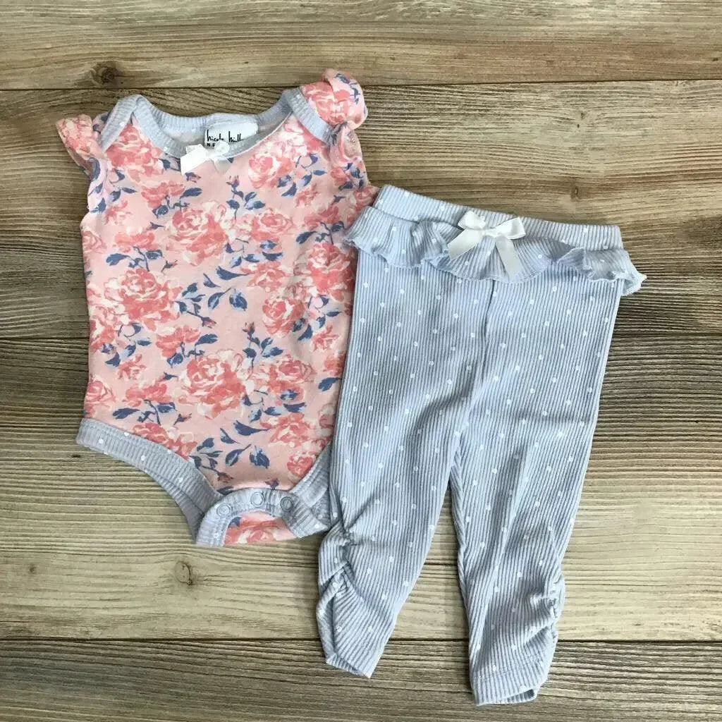 Flat lay of Nicole Miller 2-piece floral baby outfit: pink bodysuit and blue striped ruffle-waist leggings on wood