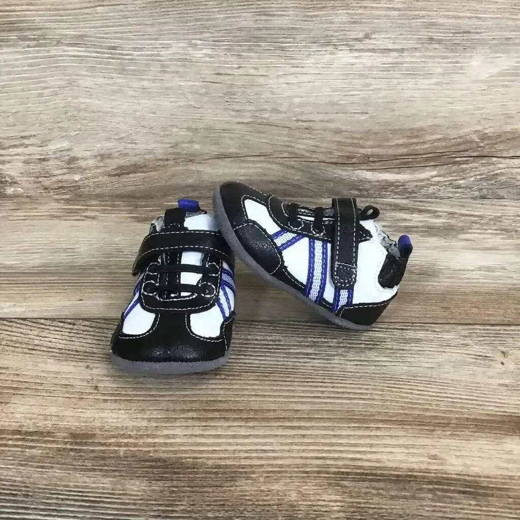Top down view of Robeez Leather Velcro Sneakers size 3-6m showcasing black and white leather with blue stripe accents on wood plank floor