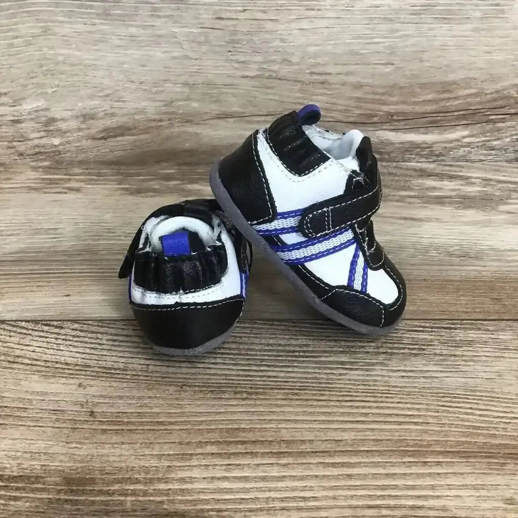 Three-quarter view of Robeez baby leather sneakers 3-6 months showcasing black and white leather with purple stripe and Velcro strap on wood background