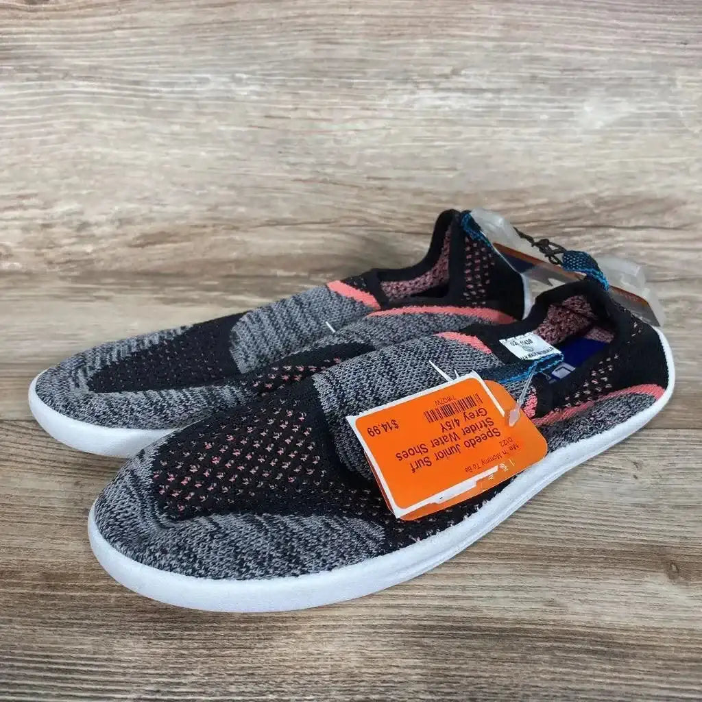 Angled side view of grey and black Speedo Surf Strider water shoes with pink accents, slip-on knit upper and white sole on wood