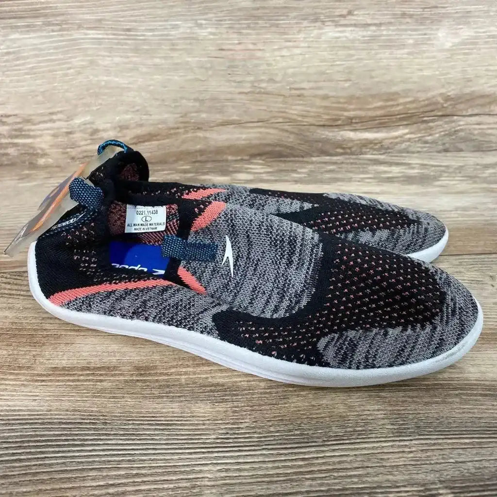 Side view of Speedo Junior Surf Strider water shoes in grey, black, and coral showing slip-on knit upper, pull tab, and white sole on a wood background
