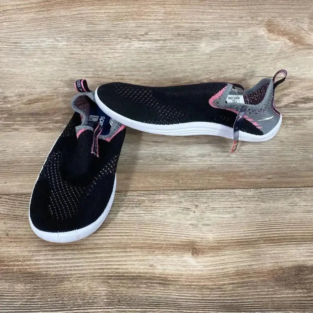 Angled view of black Speedo Junior Surf Strider water shoes with pink accents and white soles on a wood-grain background