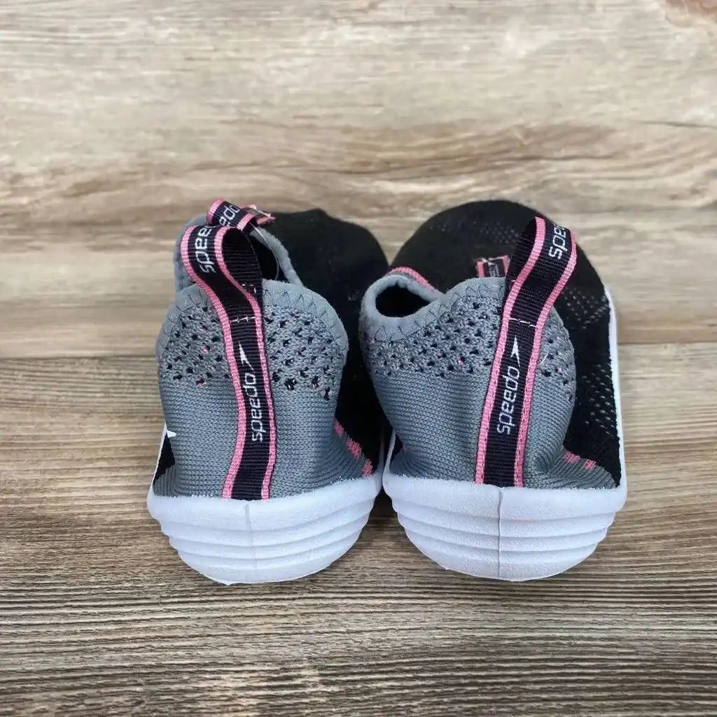 Rear view of gray and black Speedo Junior Surf Strider water shoes with pink accents, pull loops, and white outsoles on wood