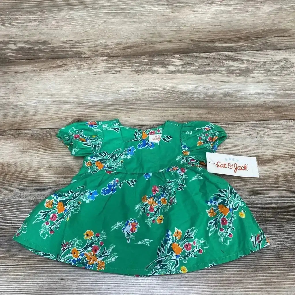 Flat lay of NWT Cat & Jack Floral Short Sleeve Dress size Newborn showcasing green fabric with multicolor floral print and brand hangtag on wood plank floor