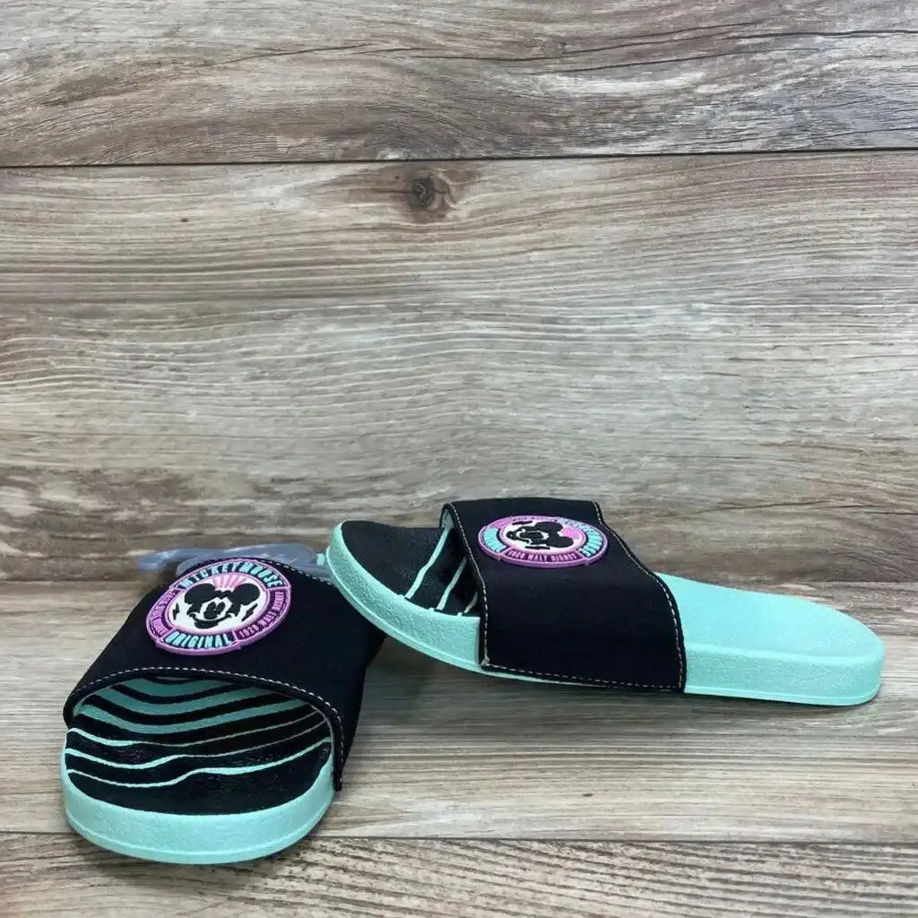 Angled front view of Mickey Mouse slides showing mint footbed, black strap with pink Mickey patch on wood backdrop