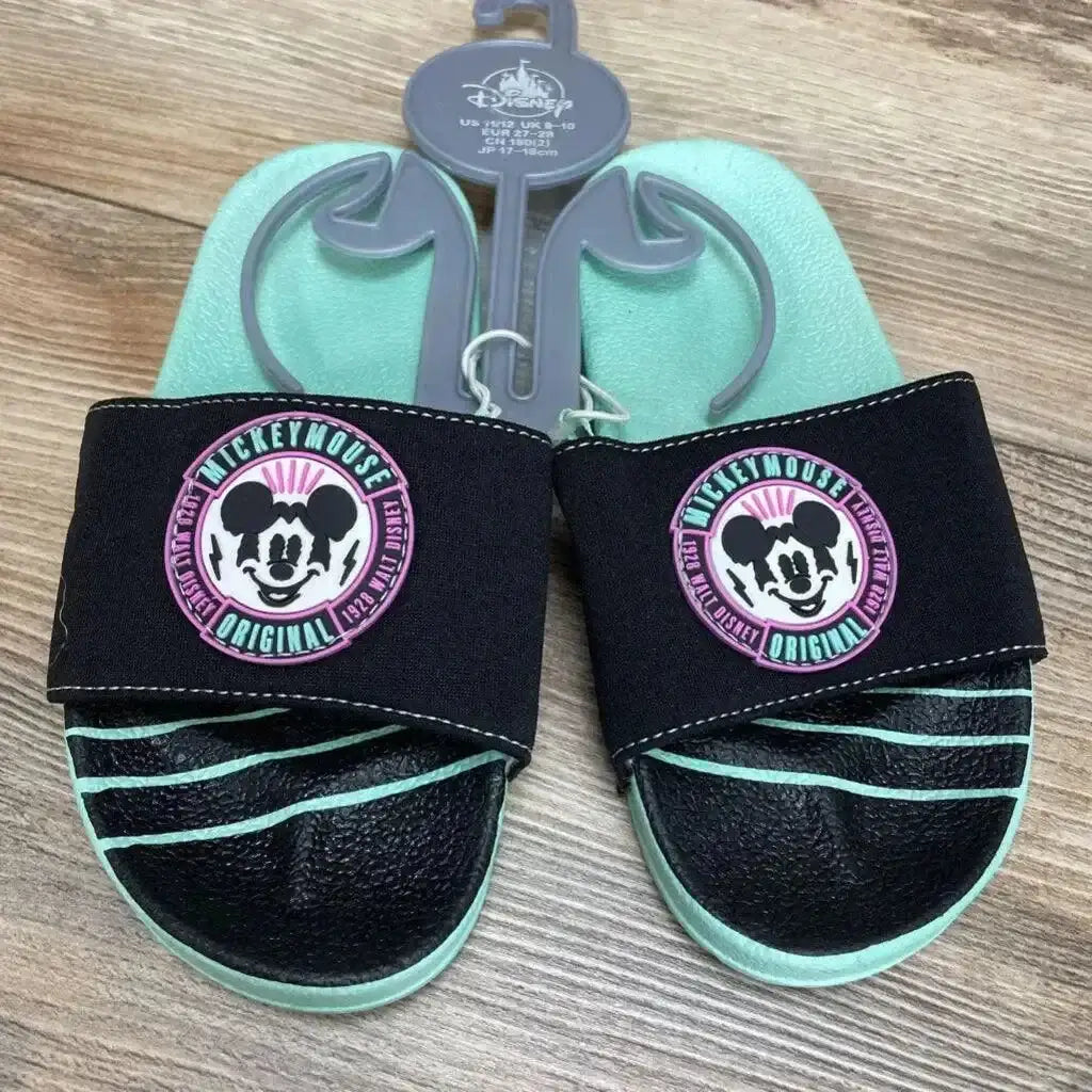 Top view of toddler mint and black Mickey Mouse slide sandals, size 11/12C, showing round Mickey patches on the straps on a wood floor