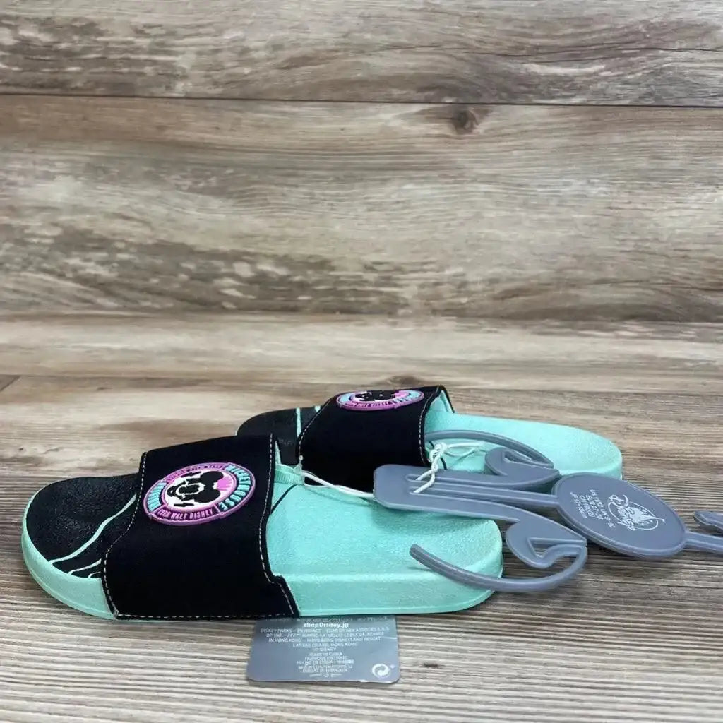 Side view of mint-green slide sandals with black strap featuring Mickey Mouse patch and tags on wood floor