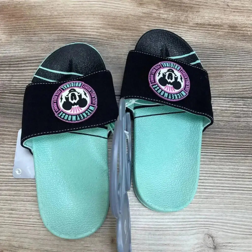Top view of mint green Mickey Mouse slide sandals showcasing black strap with round Mickey patch on wood background