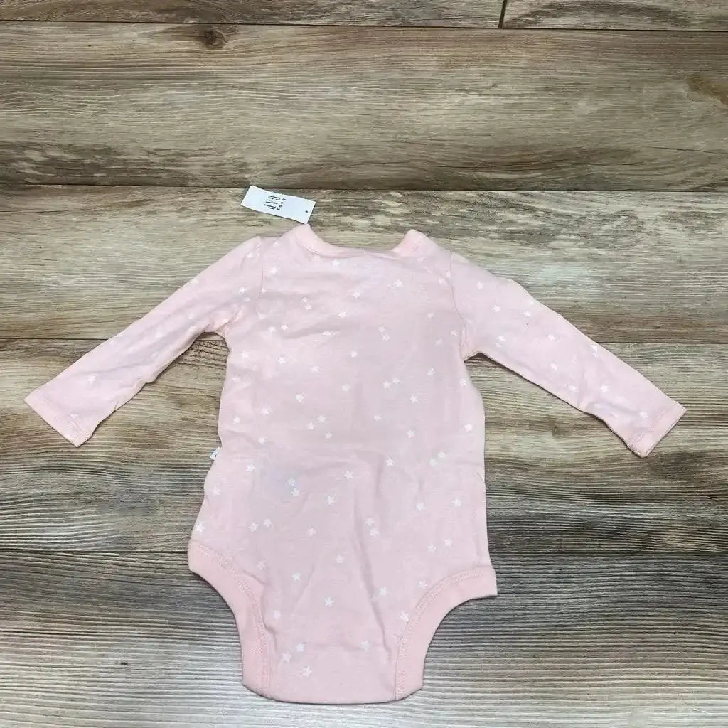 Flat lay of BabyGap pink kimono-style long-sleeve bodysuit with white star print and size tag on wood background