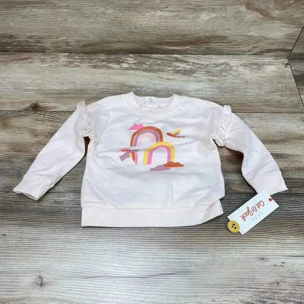 Flat-lay front view of pink Cat & Jack baby sweatshirt (6–9m) showing rainbow-and-cloud print and ruffle shoulders on wood floor