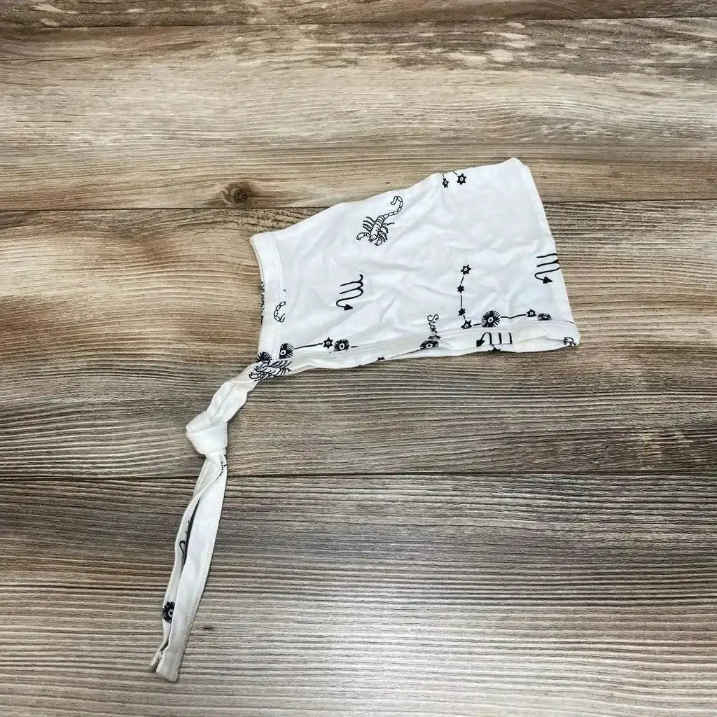 Top-down view of ivory Kate Quinn baby elf hat (6 to 12 months) showcasing black Scorpio zodiac prints and knotted strap on wood background