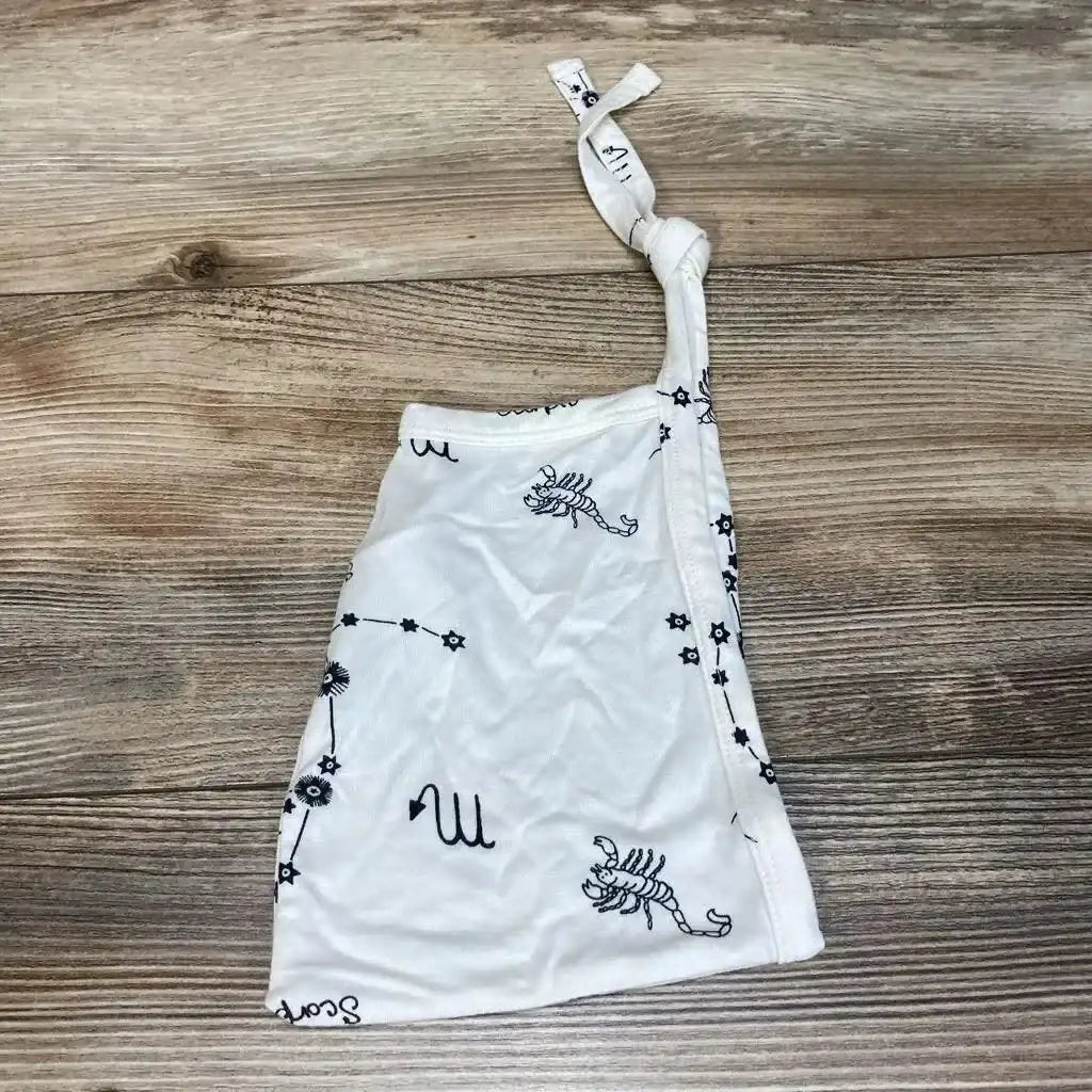 Flat lay of Kate Quinn ivory Scorpio elf hat showing knotted top and scorpion constellation print on wooden surface
