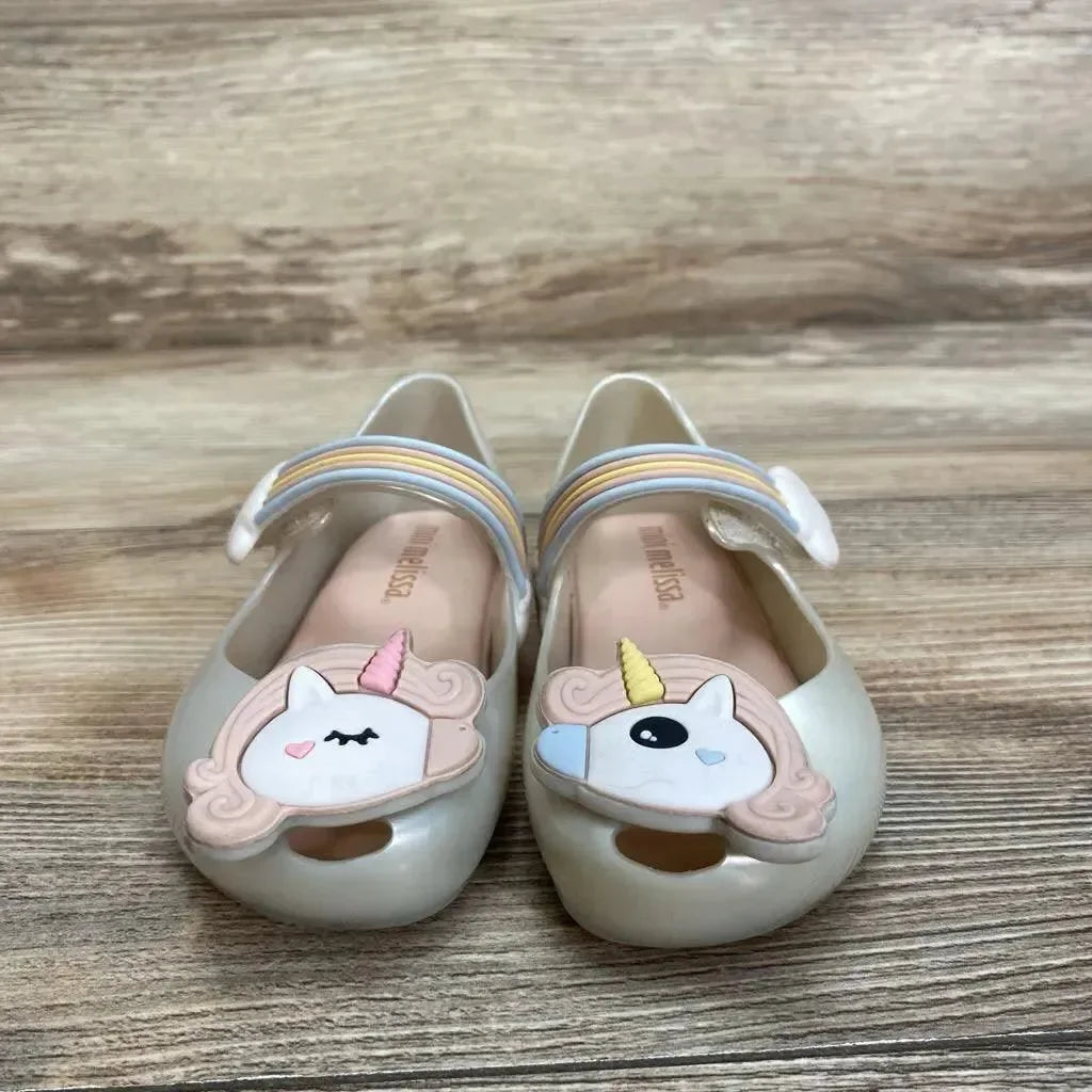 Front view of ivory Mini Melissa Mary Jane shoes size 6C with unicorn appliques and rainbow straps on wood floor