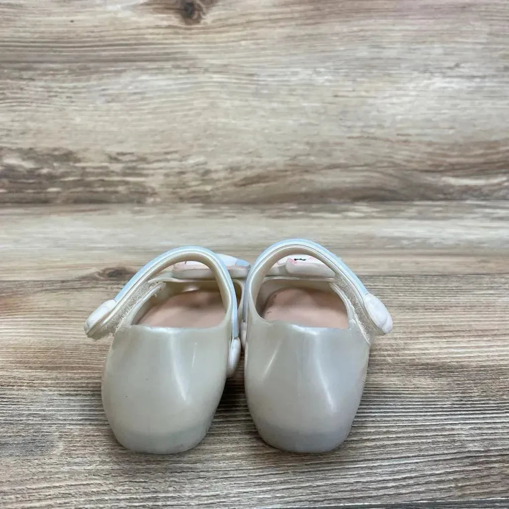 Rear view of ivory Mini Melissa Mary Jane shoes, size 6C, showing glossy finish and unicorn strap on wood background