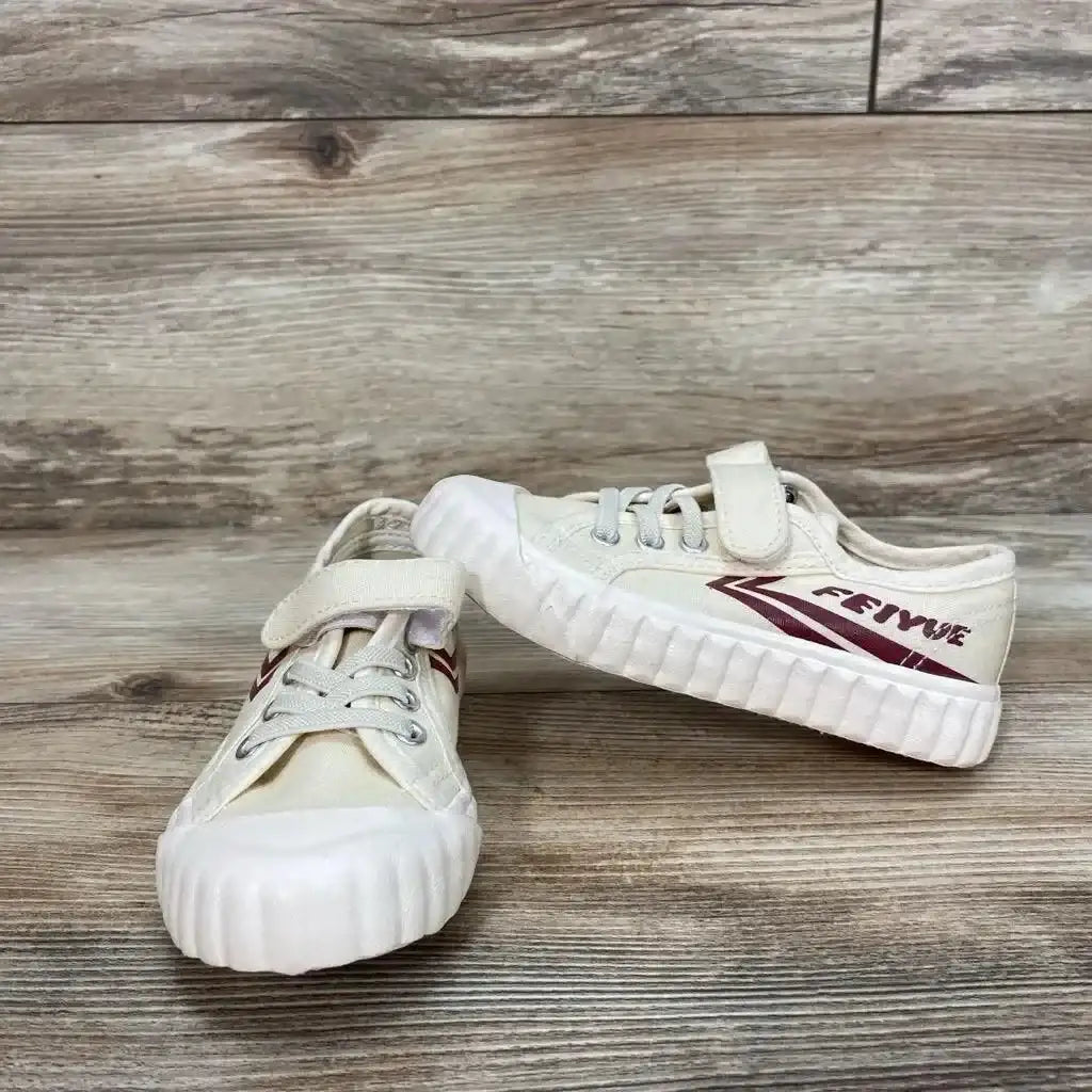 Front view of tan Feiyue toddler shoe with velcro strap, maroon side logo and white rubber toe on wood floor