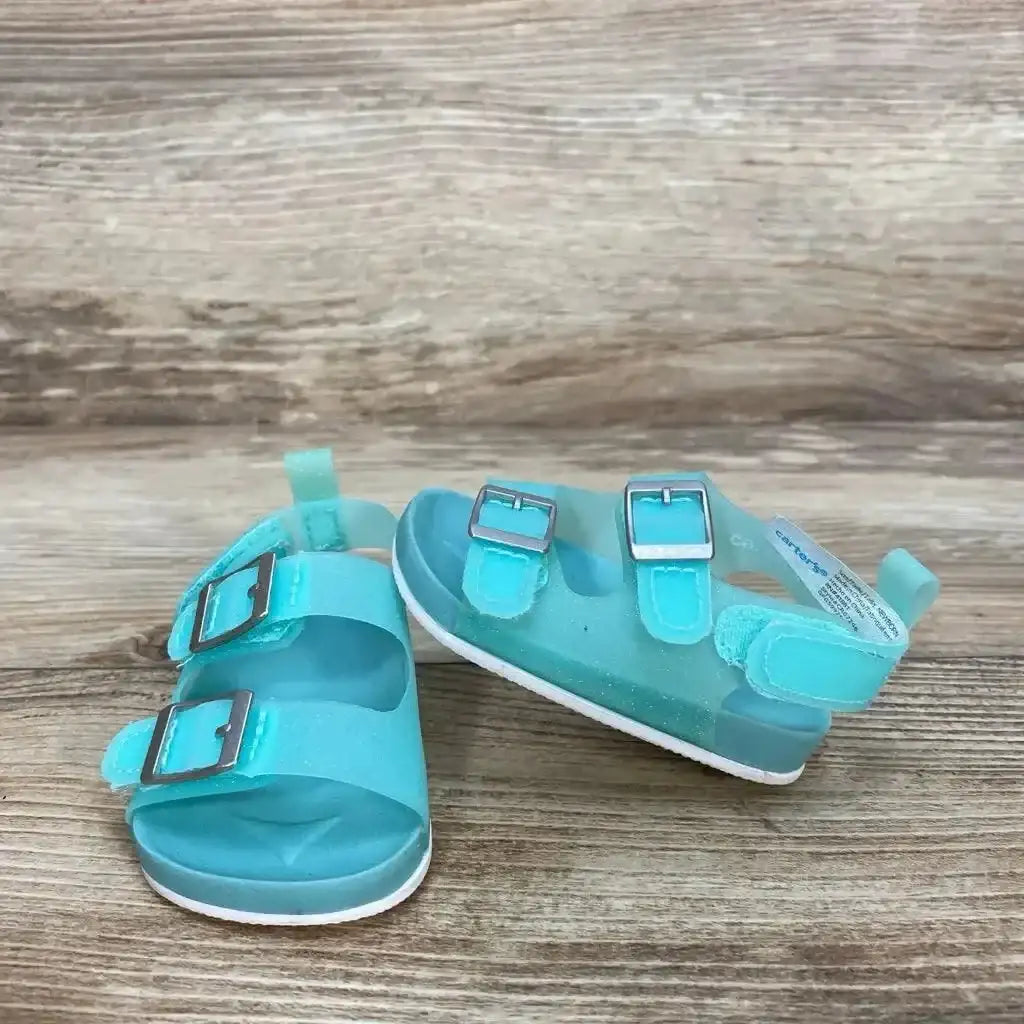 Front view of teal Carter's newborn jelly sandals with two buckle straps and white sole on wood background