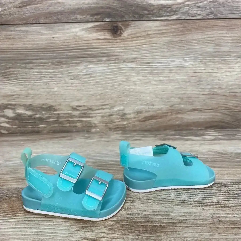 Side view of newborn teal Carter's jelly sandals showing two buckle straps, Velcro heel strap and white sole on wood background