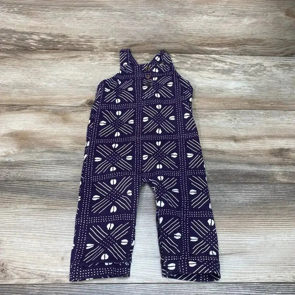 Flat lay of purple ade + ayo baby overalls showcasing white geometric print and button shoulder straps on wood background