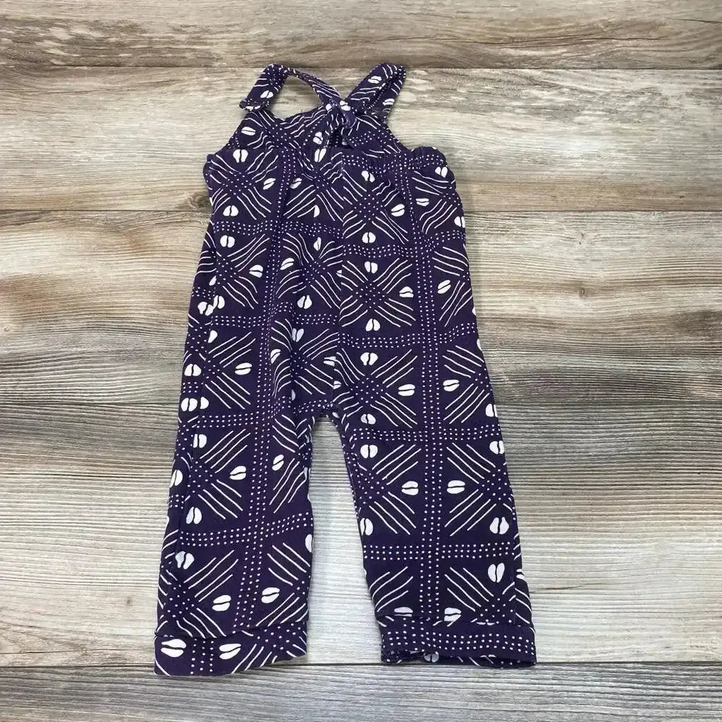 Top view of purple baby overalls (0-3M) with white geometric print and crossed straps on light wood background