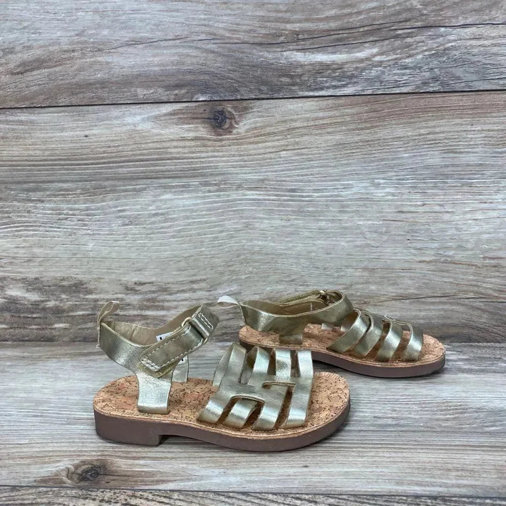 Three-quarter view of OshKosh Raquel toddler sandals 5C with gold straps, cork footbed and ankle Velcro on wood background