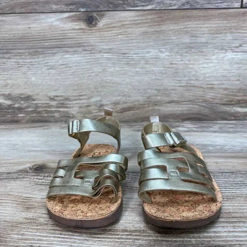 Front view of OshKosh Raquel toddler sandals, metallic gold size 5C, showing cork footbed and velcro ankle straps on wood background