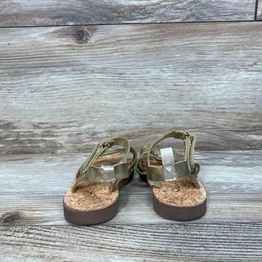 Rear view of OshKosh Raquel toddler sandals showing cork footbed and metallic gold straps on wood background