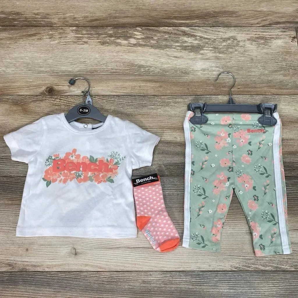 Flat lay of Bench baby set: white tee with coral floral logo, mint floral leggings with side stripes, pink dot sock on wood, size 0-3M visible