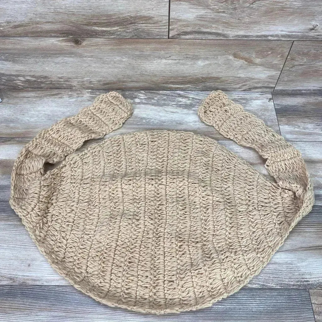 Top-down view of beige crocheted newborn hammock with round padded center and two straps on wood background
