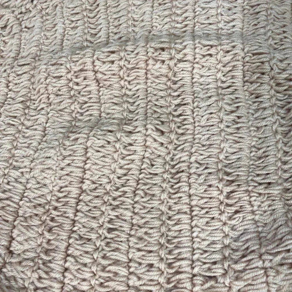 Close-up of beige hand-knitted newborn photography hammock showing ribbed texture and stitch detail on plain background