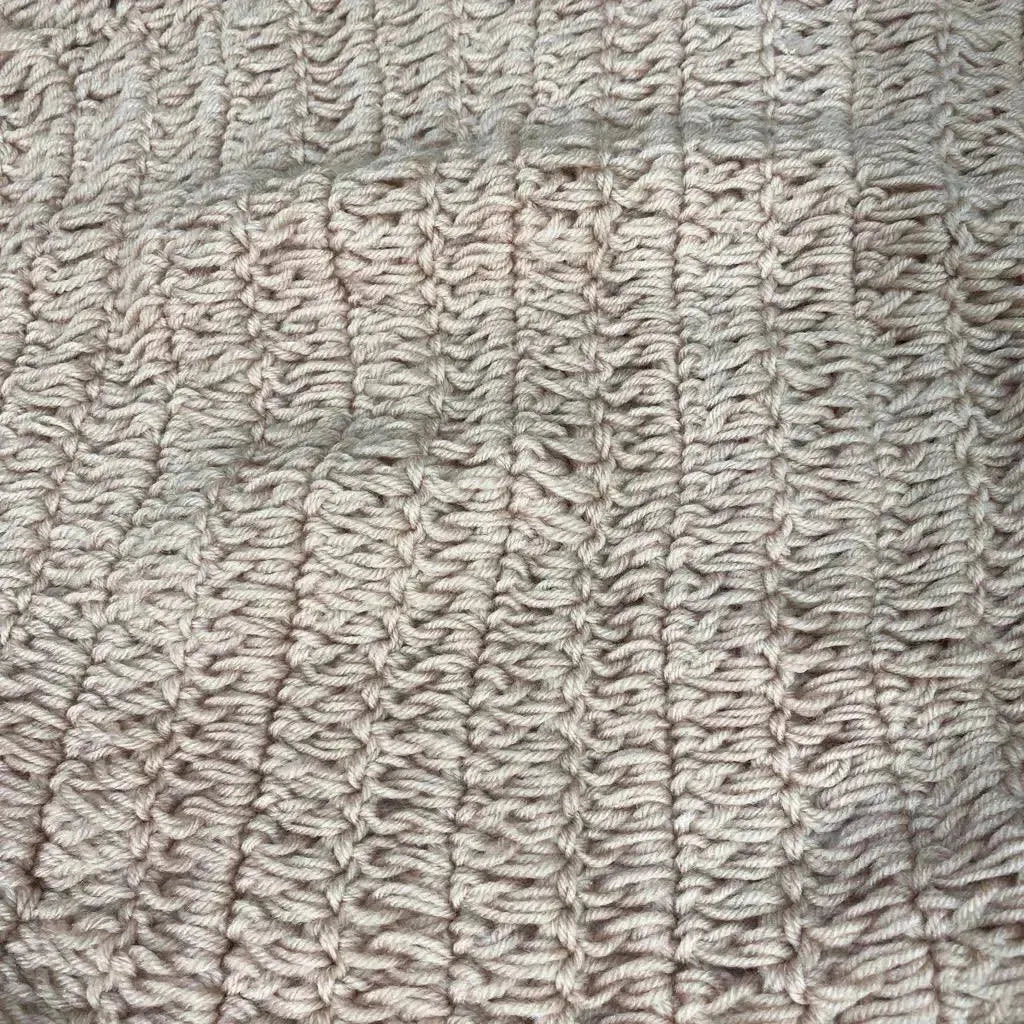 Close-up of beige hand-knitted newborn photography hammock showing ribbed texture and stitch detail on plain background