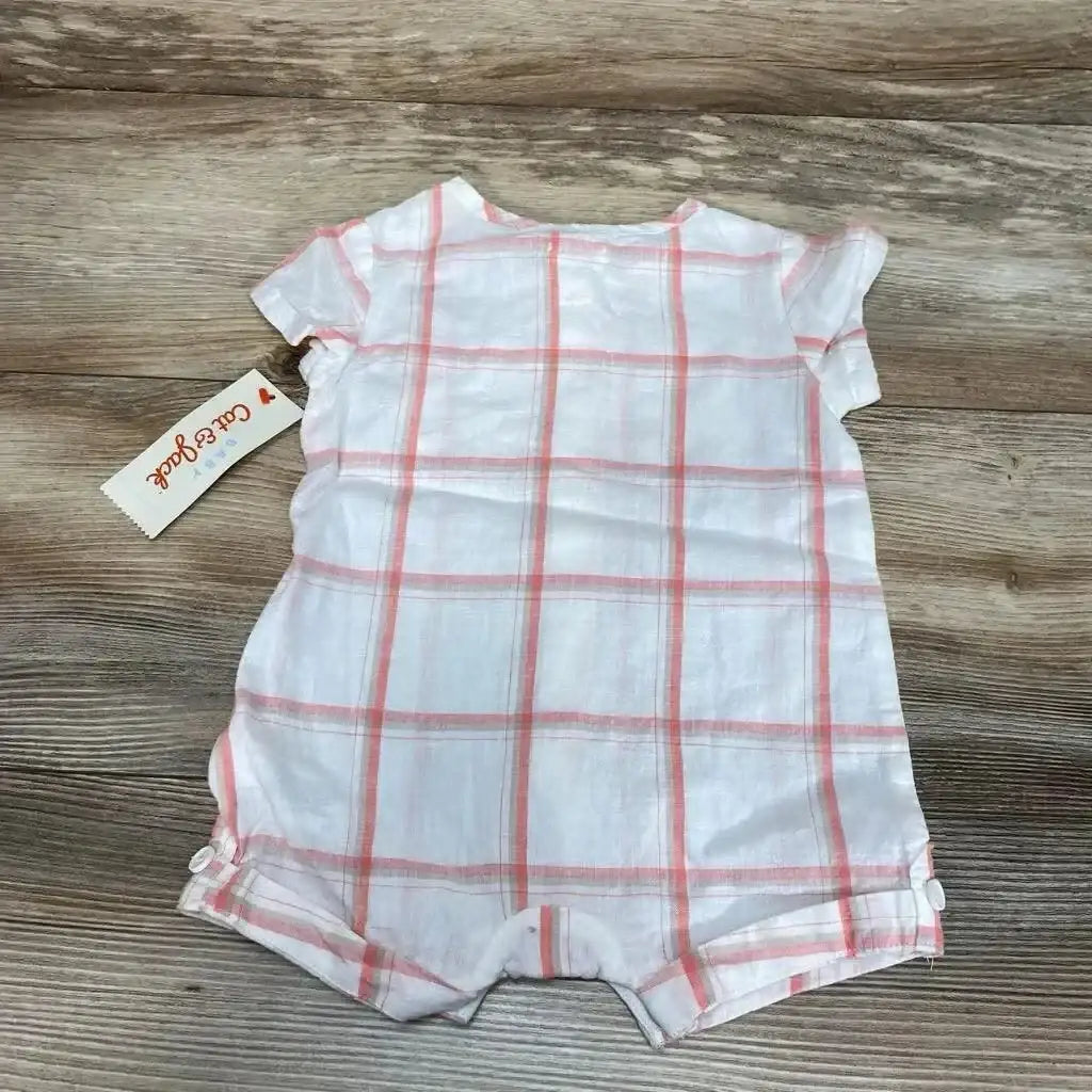 Flat lay of white baby shortie romper with pink plaid print showing short sleeves and snap closures at legs on wood background