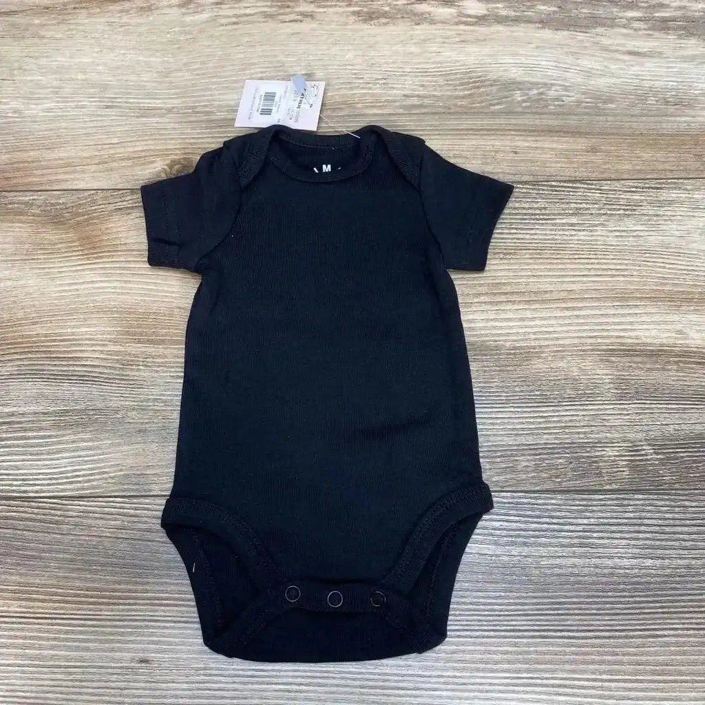 Top-down view of black organic cotton newborn bodysuit showcasing envelope shoulders and three-snap crotch on light wood background